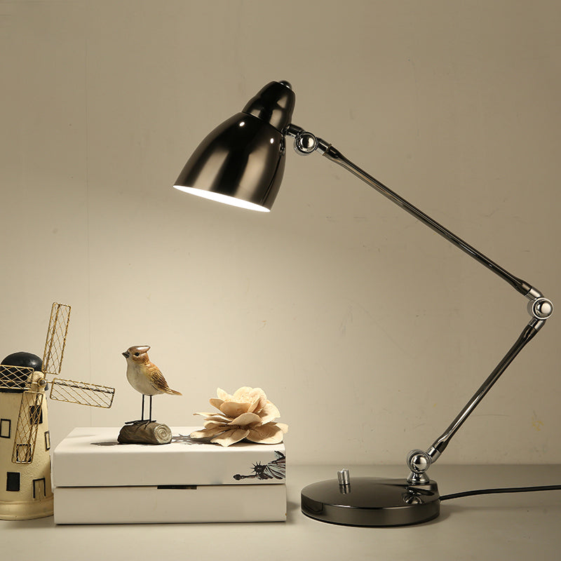 Schwarze Architektenlampe mit Gelenkarm neben Deko-Elementen auf hellem Tisch