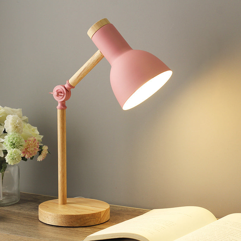 Rosafarbene Lampe mit Holzsockel auf Nachttisch vor grauer Wand