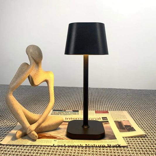 Schwarze LED-Tischlampe auf geflochtenem Tisch mit abstrakter Figur