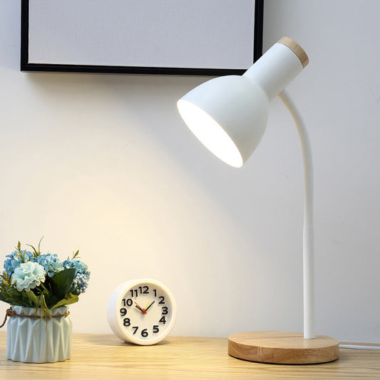 Weiße Tischlampe mit Holzsockel auf Schreibtisch neben Uhr und Blumen