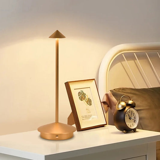 Goldene LED-Tischlampe mit konischem Schirm auf Nachttisch neben Wecker