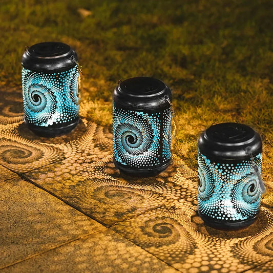 Drei solarbetriebene Gartenlaternen mit Spiraldesign werfen dekorative Muster auf den Boden