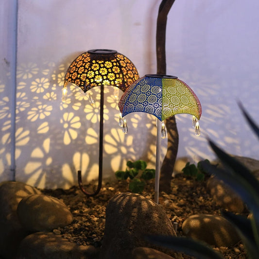 Zwei Schirm-Solarleuchten mit filigranem Muster projizieren florale Schatten im Garten

